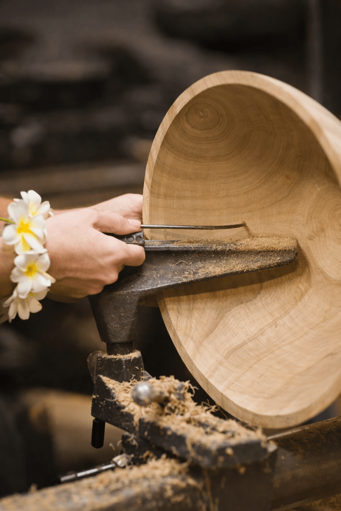 A craftsman shapes a wooden bowl on a lathe, focusing on precision. Shavings gather around the base, highlighting the woodworking process.
