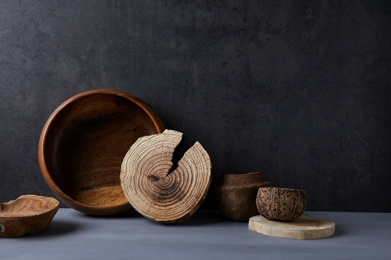 Rustic wooden bowls and natural sculptures arranged artistically on a neutral surface, highlighting organic textures and earthy tones.