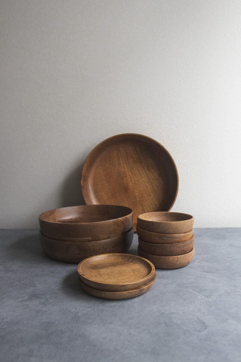 Assorted wooden bowls and plates stacked on a gray surface, showcasing natural craftsmanship and offering a rustic dining aesthetic.