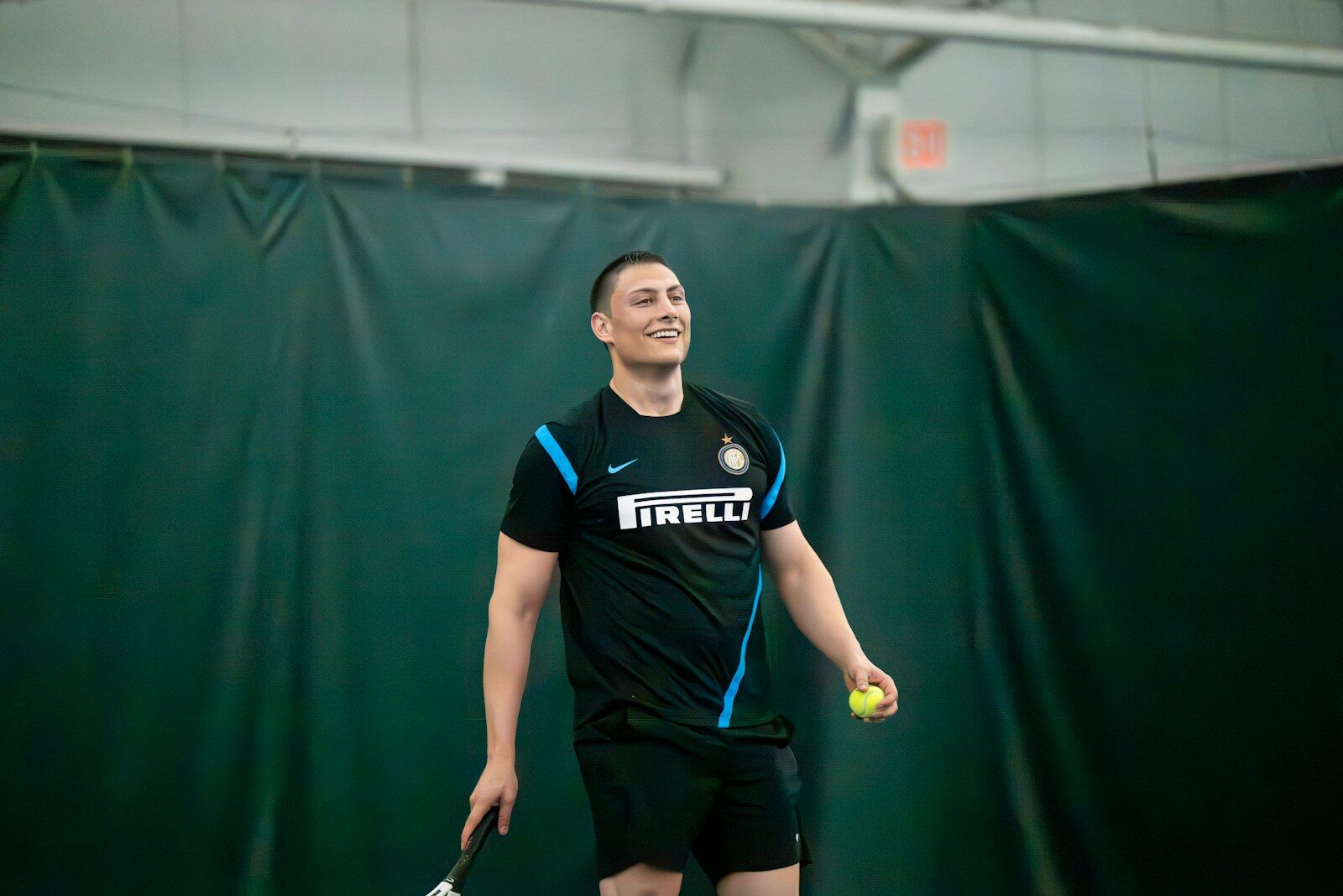 Man in black shirt playing tennis indoors